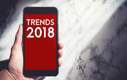 Hand holding mobile with trends 2018 on phone screen with sunlight from window at white marble wall,Business vision for new year,leave space for adding text